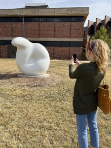 A person standing in front of a sculpture, holding their phone up to it so the Smartify app can scan and recognize it.