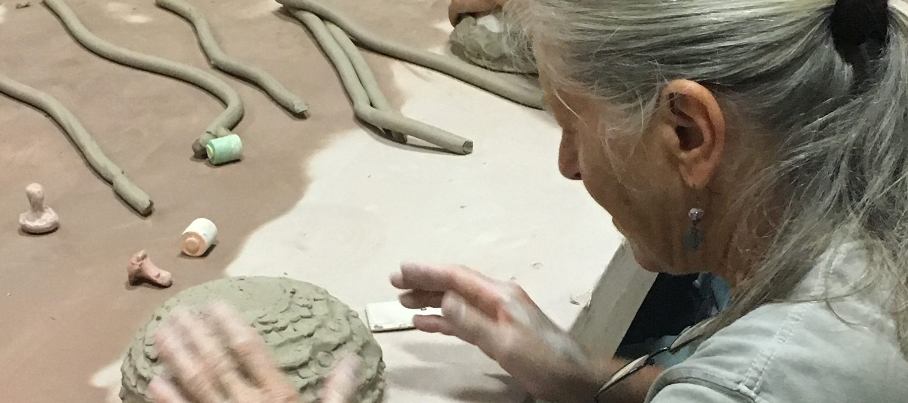 A woman with gray hair creates a bowl using clay.