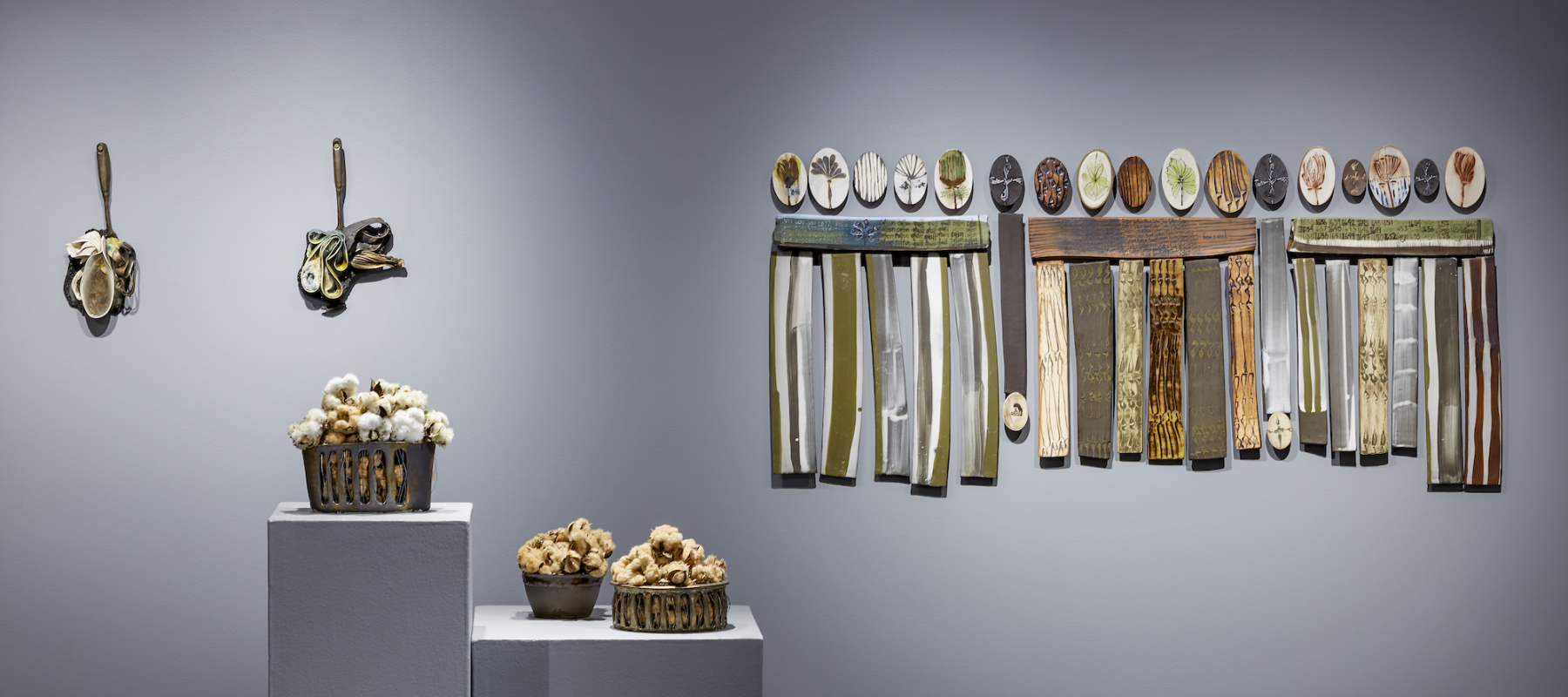 Ceramic pieces by Chotsani Elaine Dean hang on a gallery wall and sit on two pedestals.