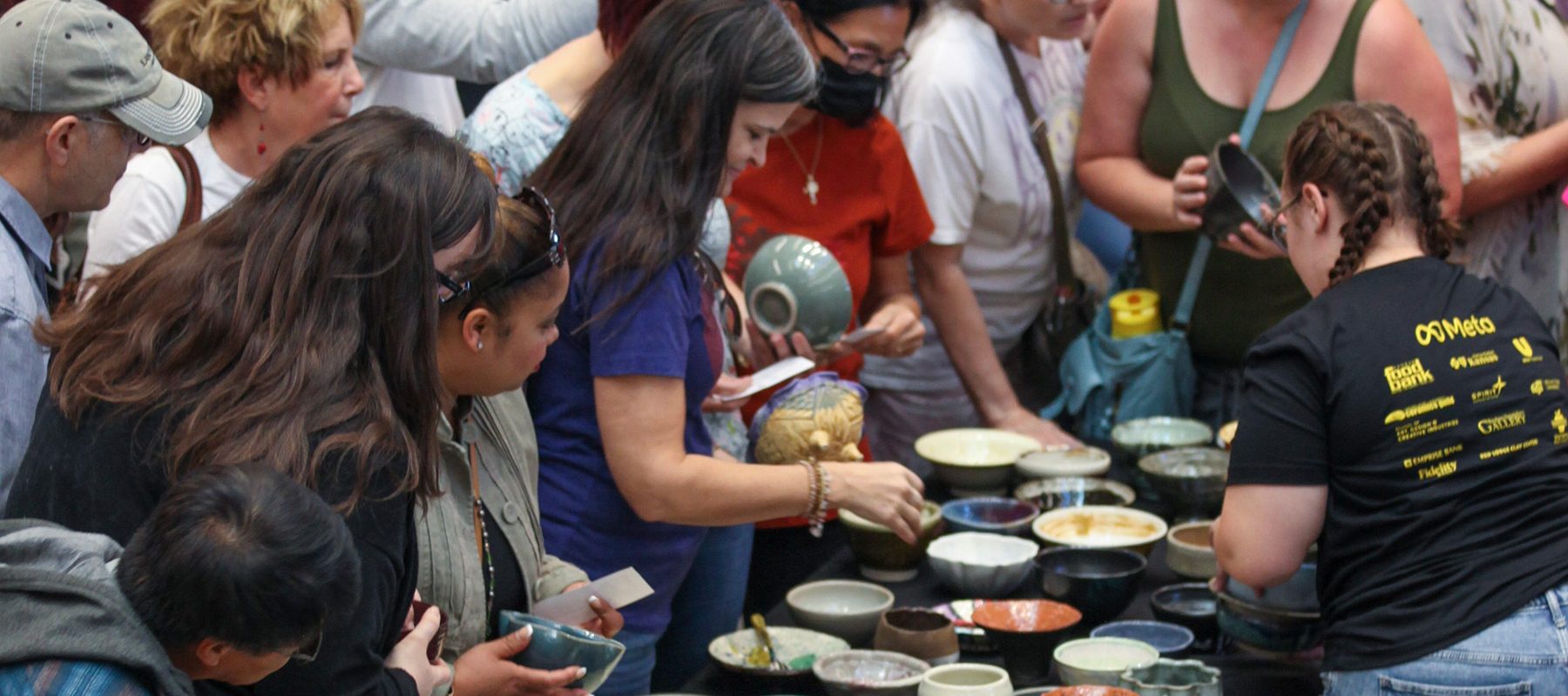 A crowd of attendees gather around a table to choose their handmade bowl at the Empty Bowls Chili Cook-Off in 2022.