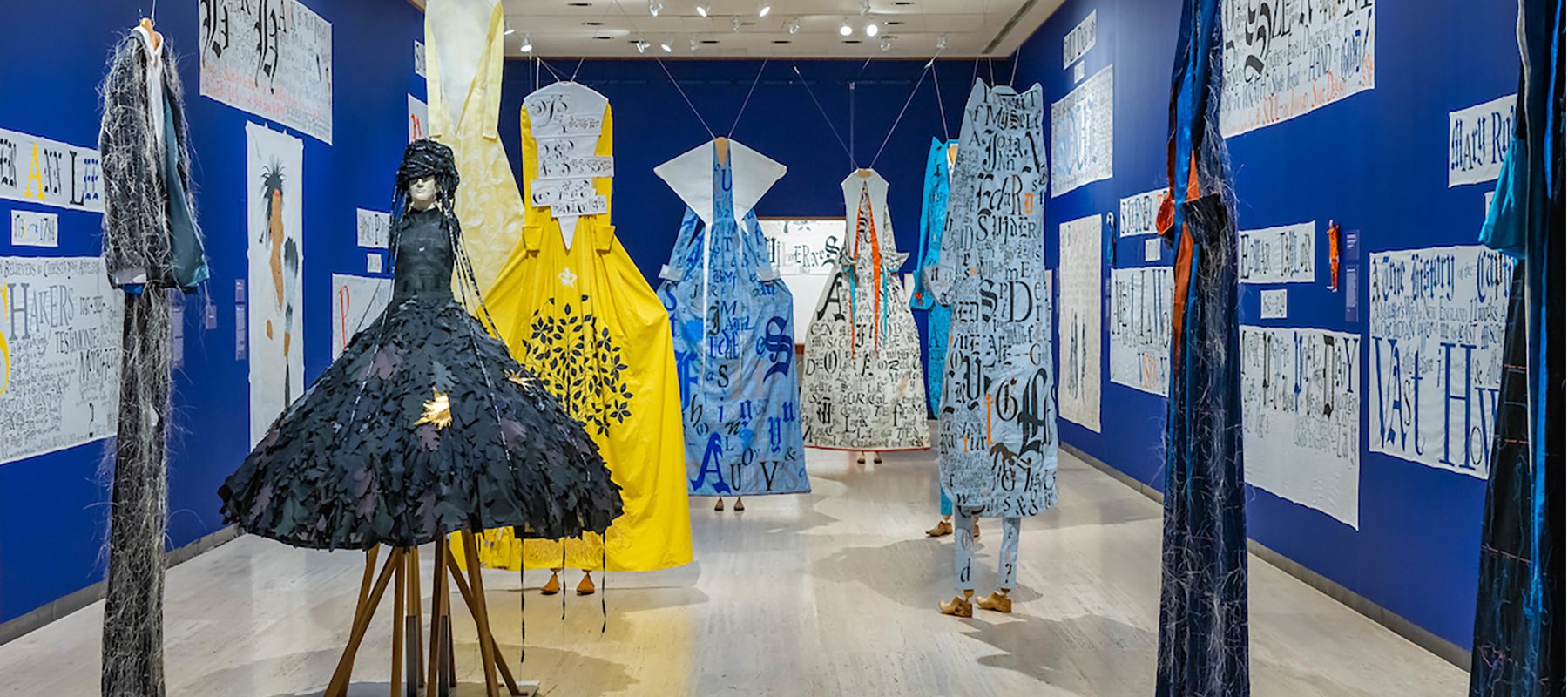 Seven sculptures shaped like dresses are positioned in a blue room.