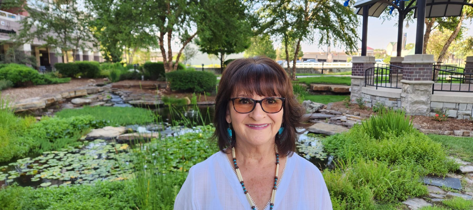 An indigenous American woman, Pauline Sharp, is pictured in front of a grassy area with trees.