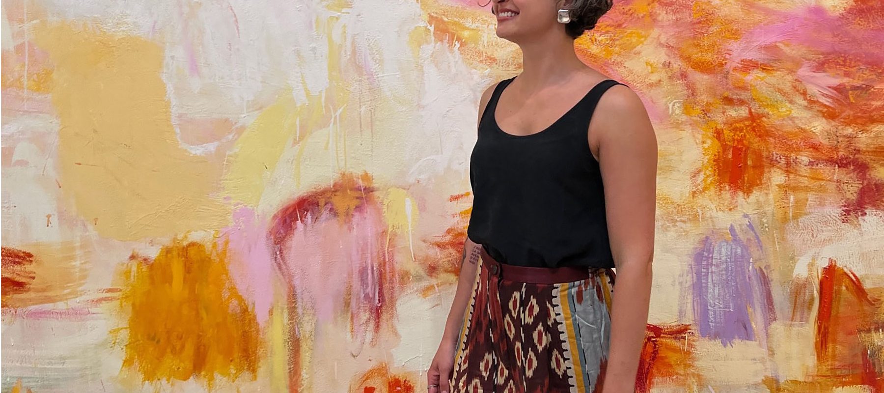 A young woman stands in front of a wall covered in a variety of colored paint.