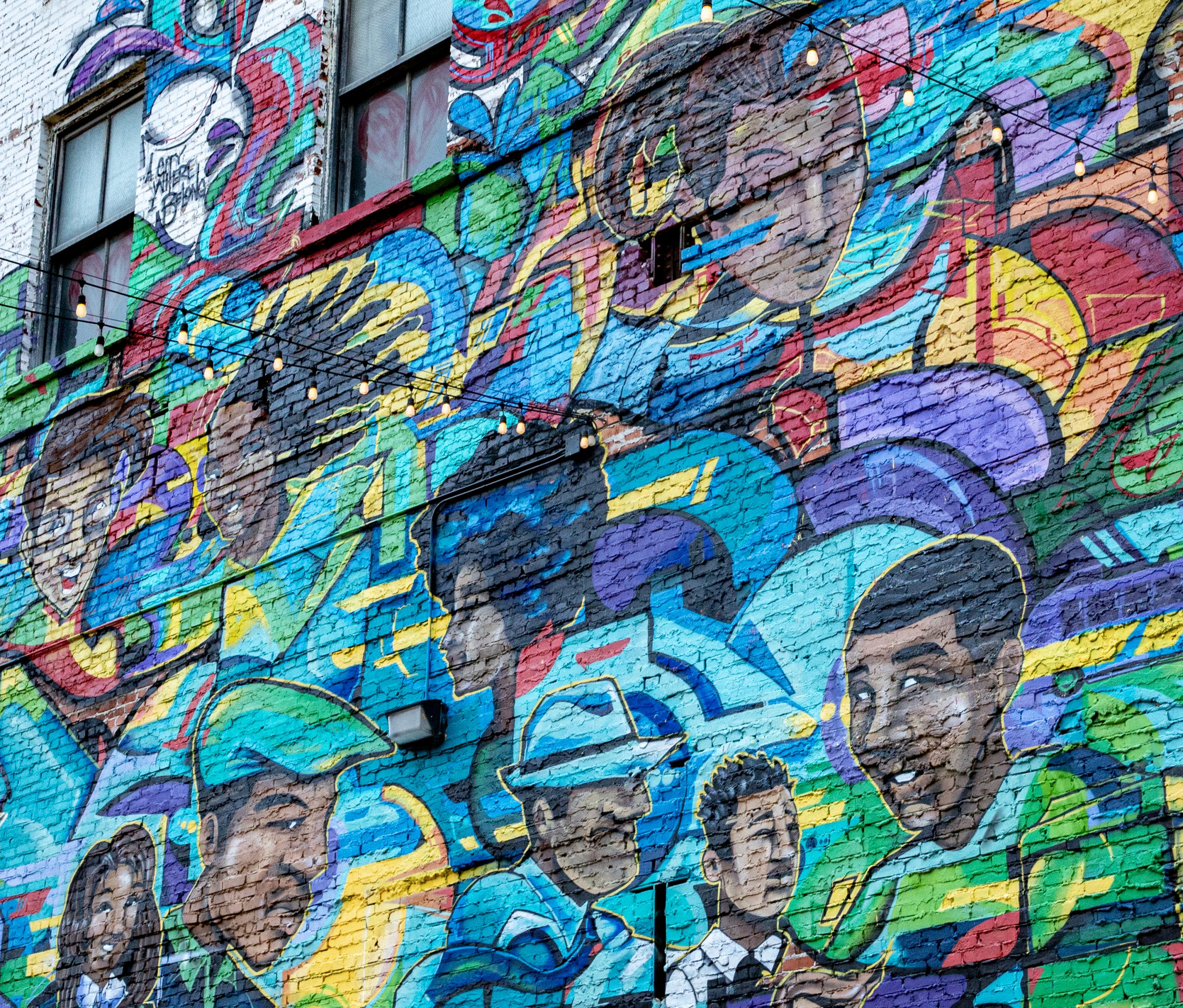 A wall is painted with images of people of all kinds, rendered in spray paint.