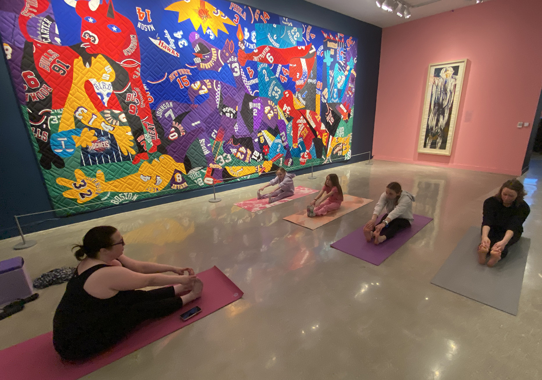 A yoga instructor leads three students in stretches in a gallery.