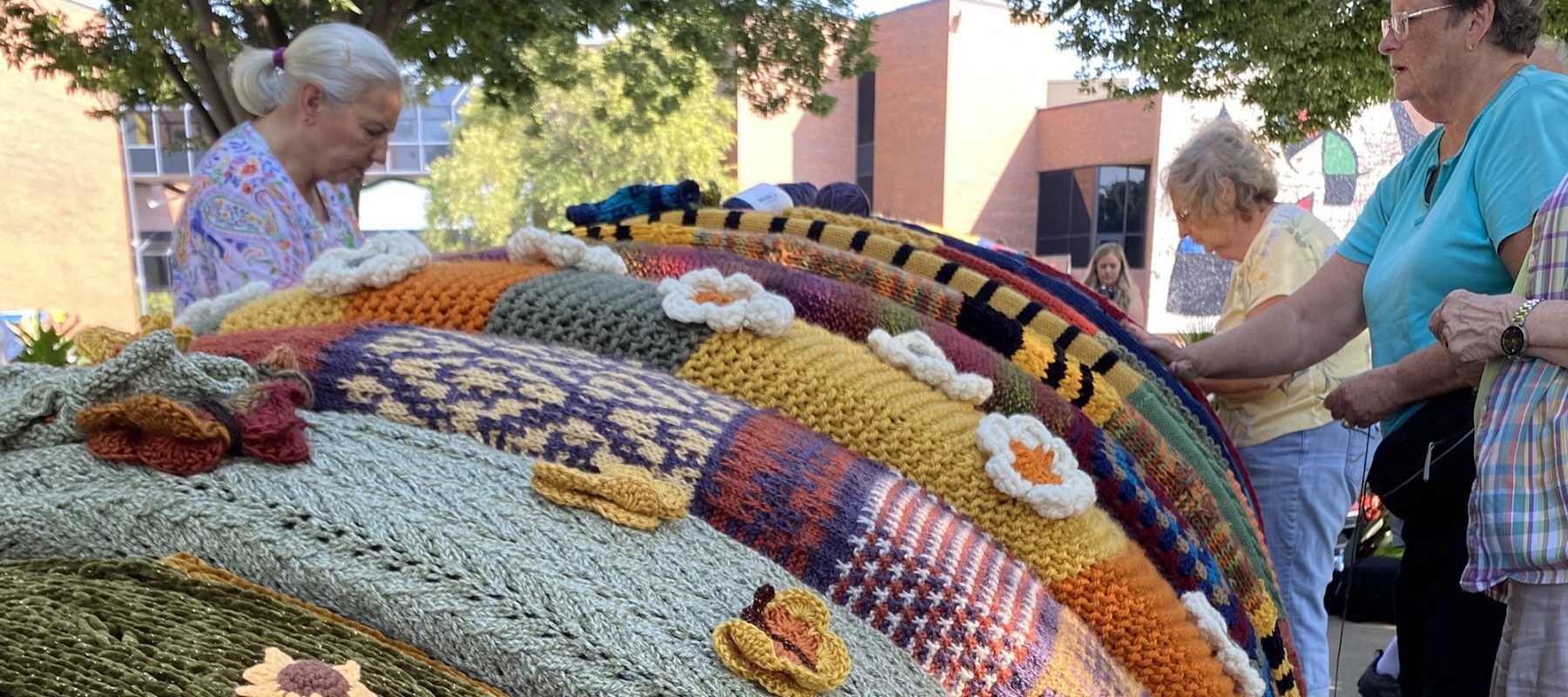 Four women attach sections of knitting to a bronze sculpture of a millipede.