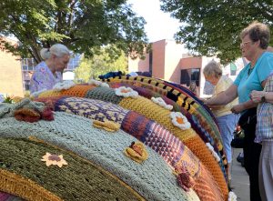 Four women attach sections of knitting to a bronze sculpture of a millipede.