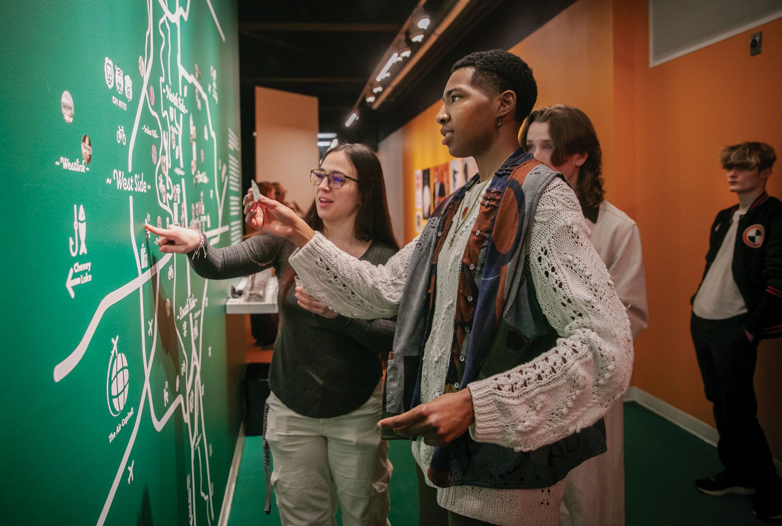 A young man applies a sticker to a large wall map of wichita