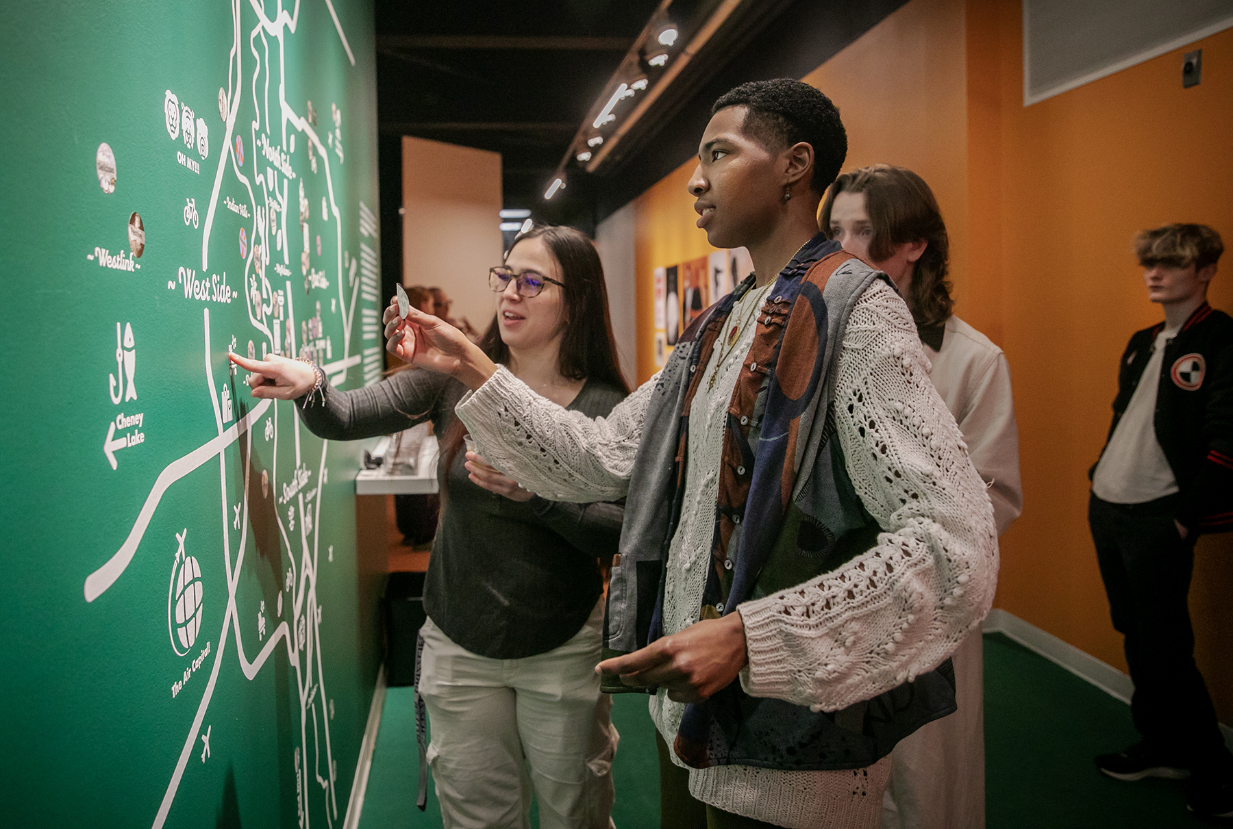 Four young people put stickers on a map that's located in the Grafly Gallery at the Ulrich.