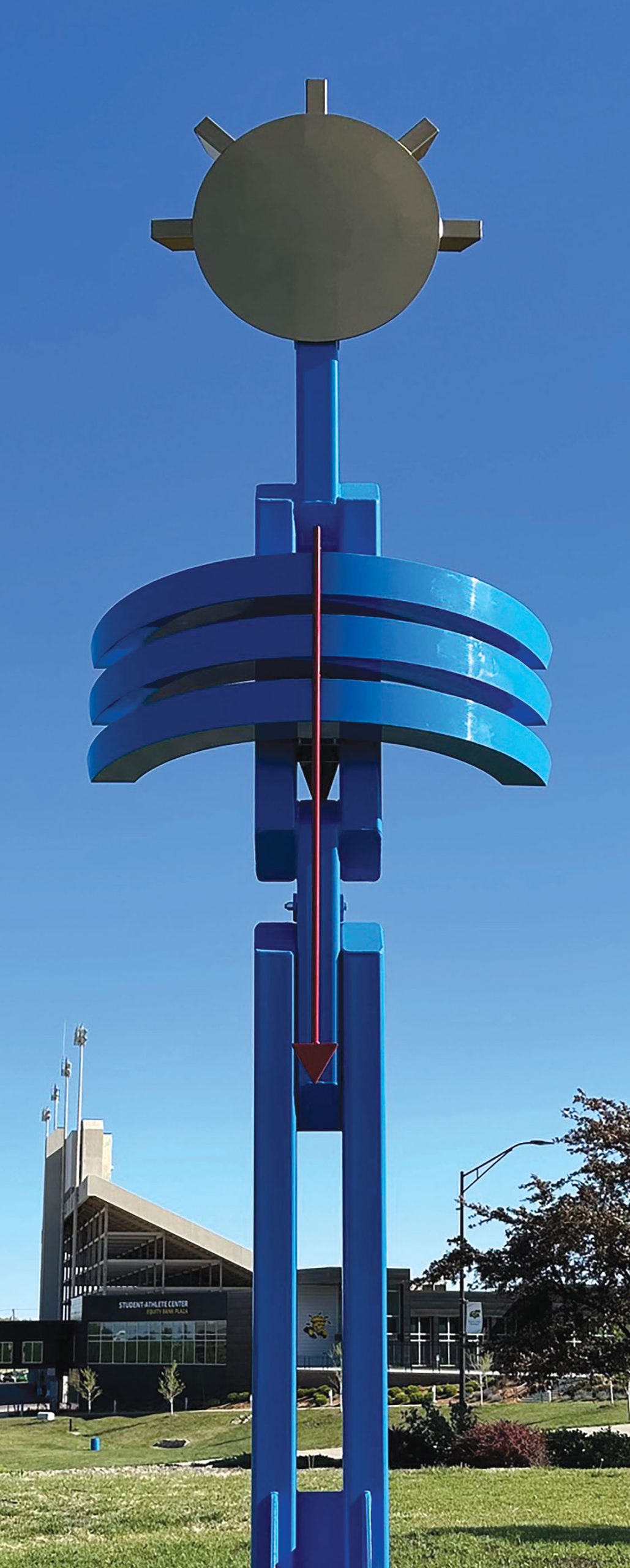 a metal sculpture with a disc at top and a pole deciding with three half circle arcs going around horizontally