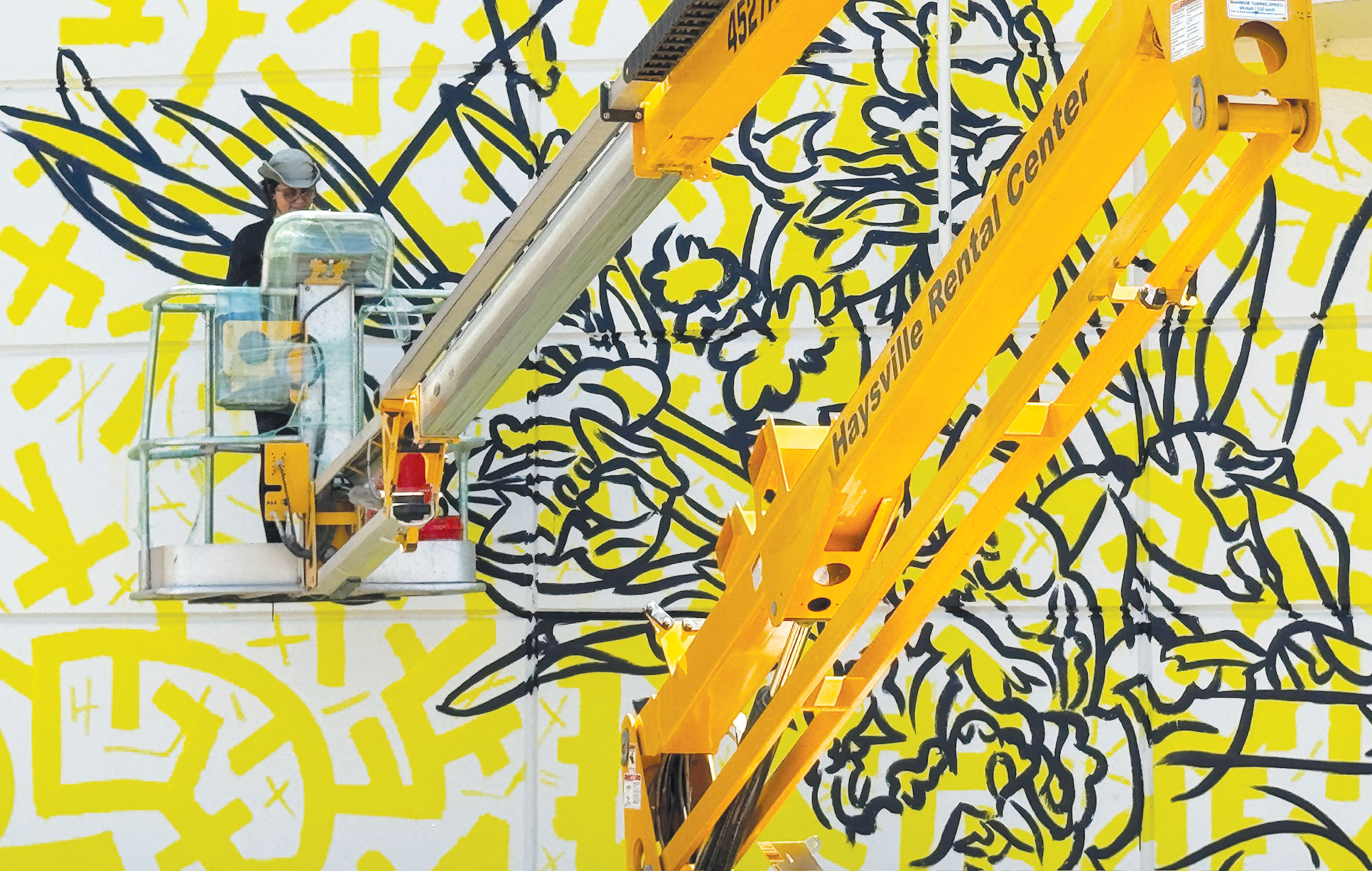 A woman in a bucket on a crane paints a vibrant mural