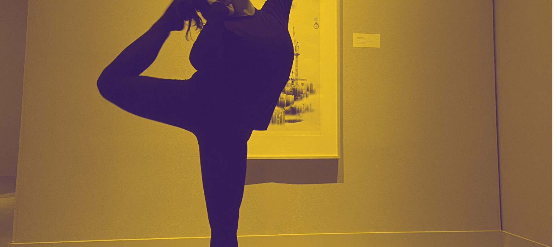 A dancer holds a pose in front of a large print in a garllery