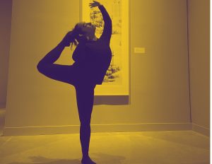 A dancer holds a pose in front of a large print in a garllery