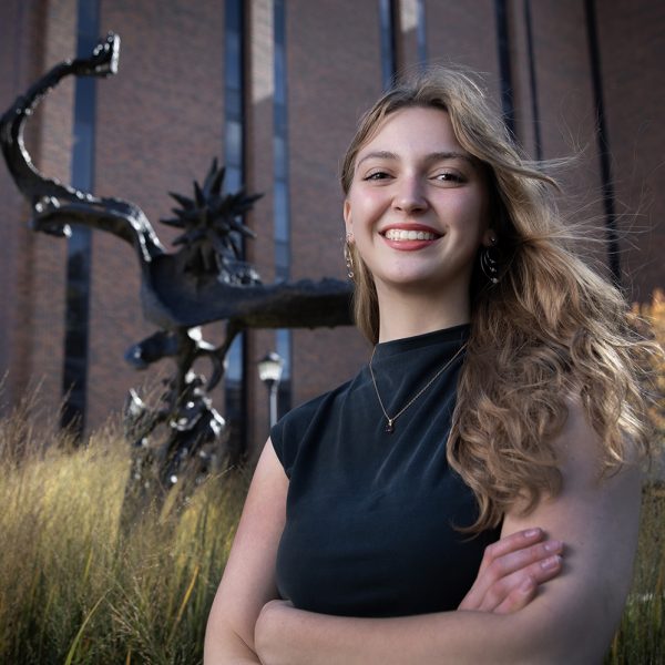 A young blond woman poses in front of a bronze sculpture.