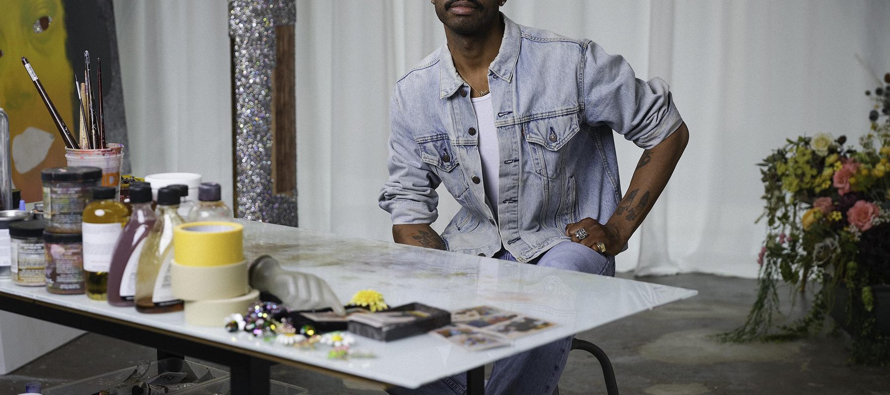 A young black male artist, Devan Shimoyama, is posed in his studio.