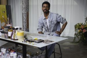 A young black male artist, Devan Shimoyama, is posed in his studio.
