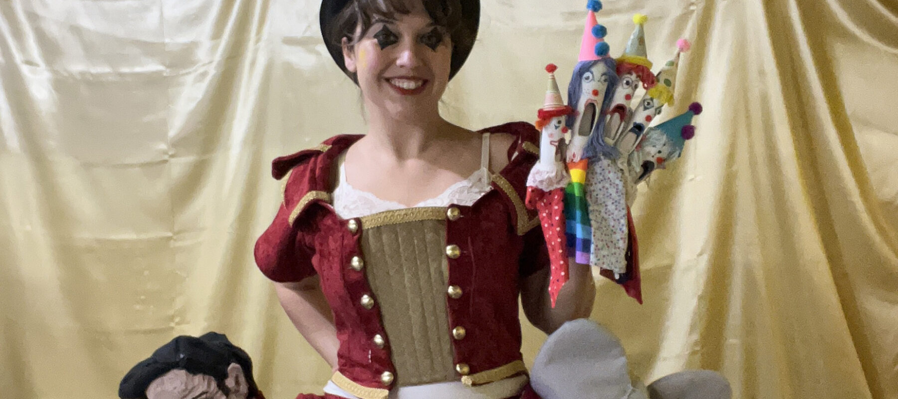 A woman in a bowler hat holds a handful of puppets.