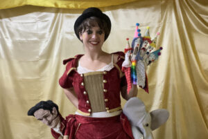 A woman in a bowler hat holds a handful of puppets.