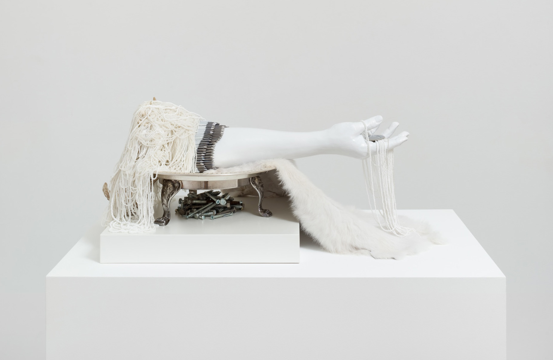 A white artwork featuring an arm, feathers, and beadwork.