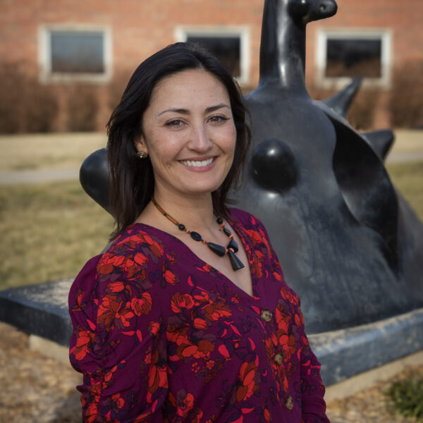 Smiling woman in a floral shirt posing in front of a sculpture.