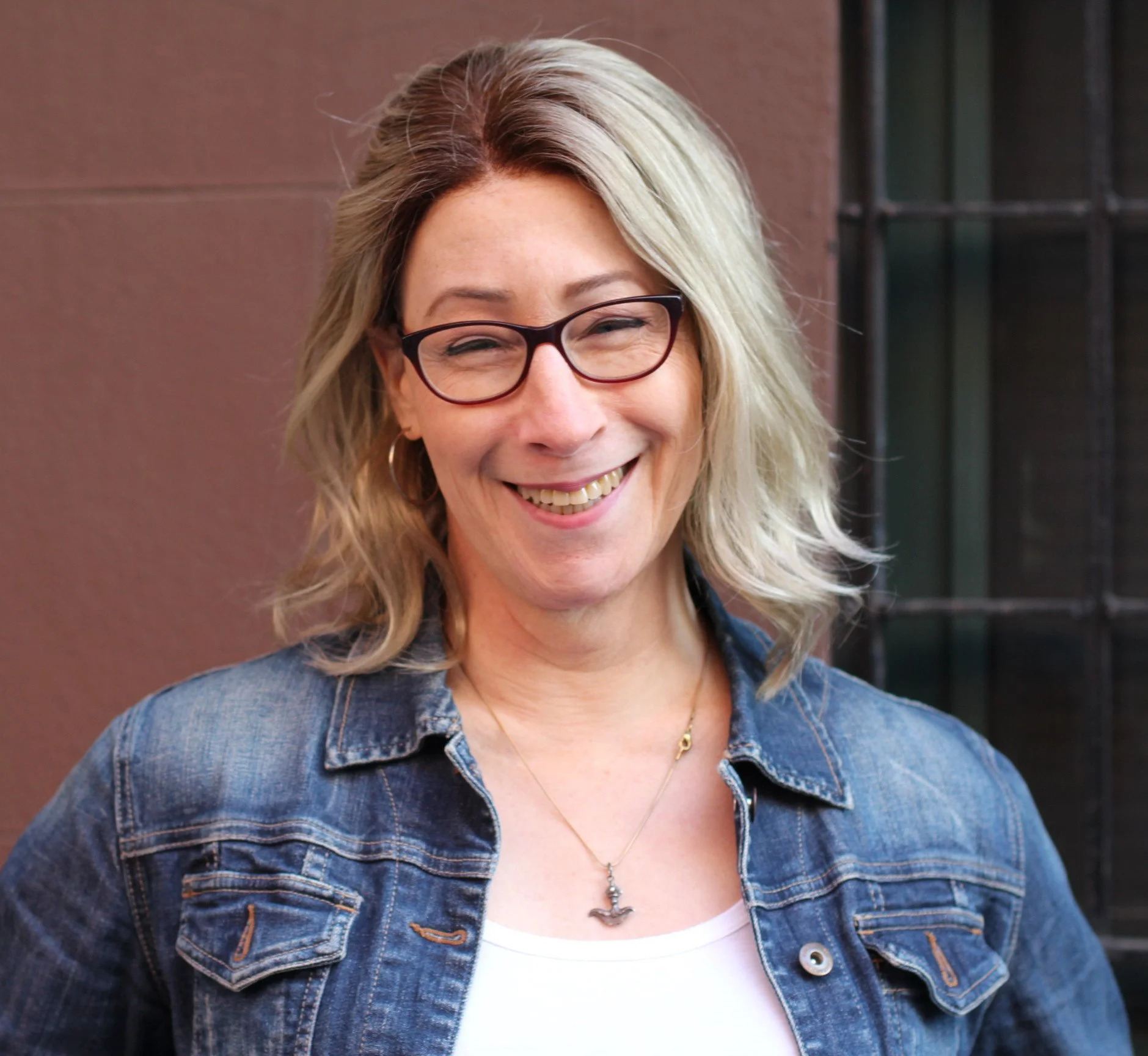A smiling blond woman in a jean jacket