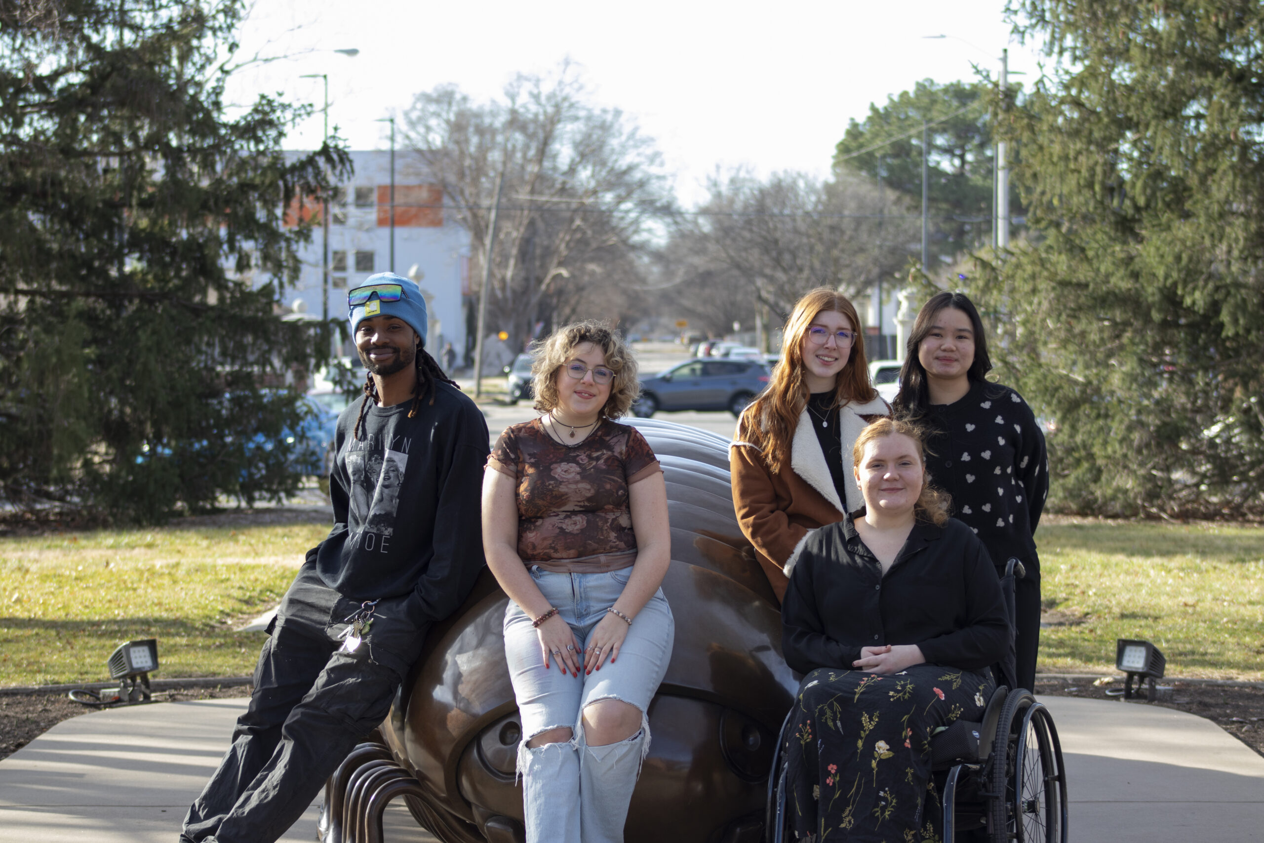 Five students pose around a statue of a centipede.