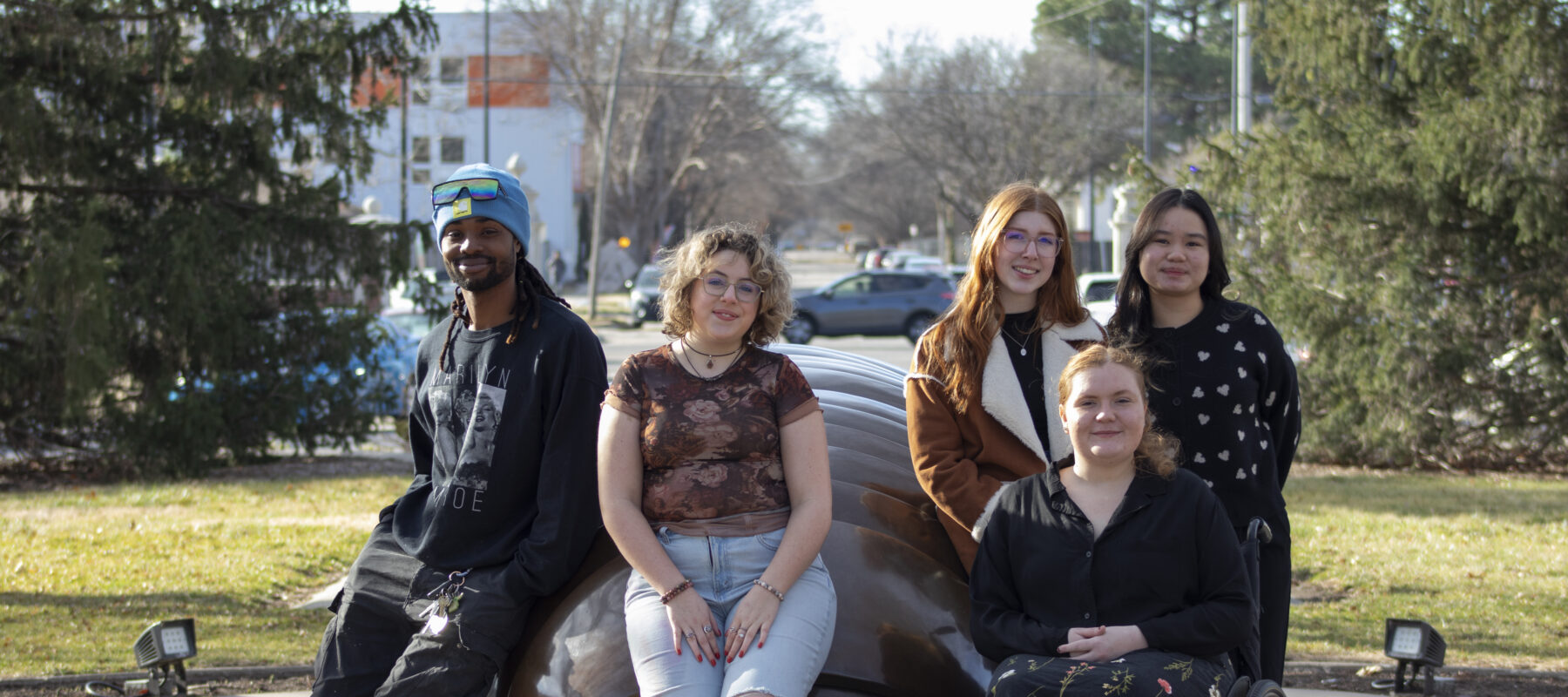 Five students pose in front of a bronze statue of a millipede.