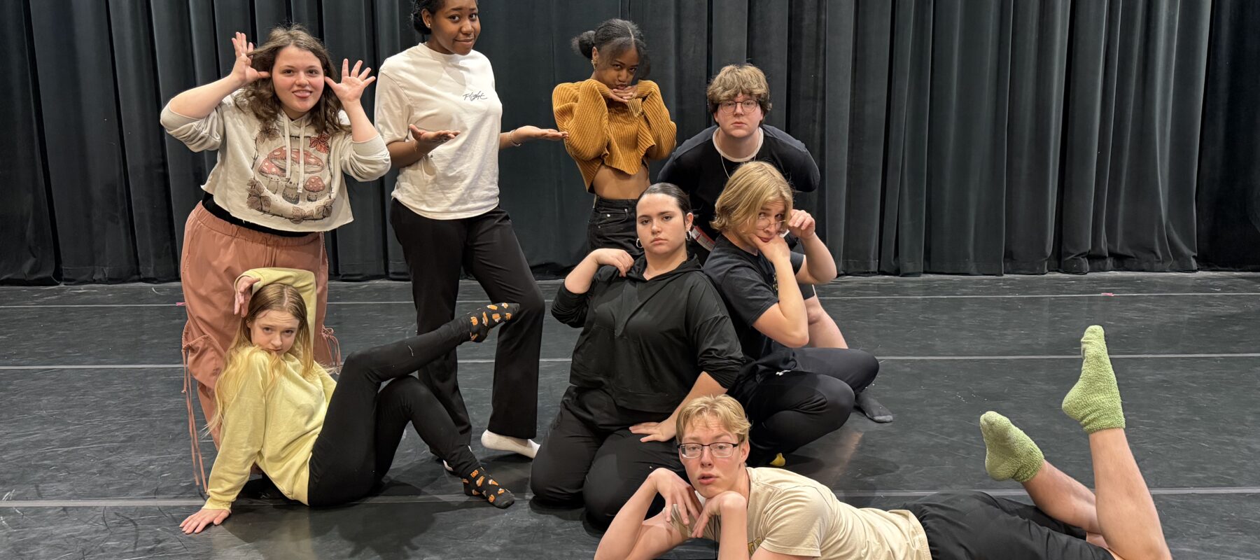 Eight improv students pose in a group on stage.