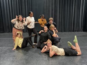 Eight improv students pose in a group on stage.