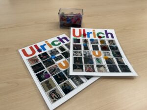 Two Ulrich branded Bingo cards and a container of tiddlywinks on a table.