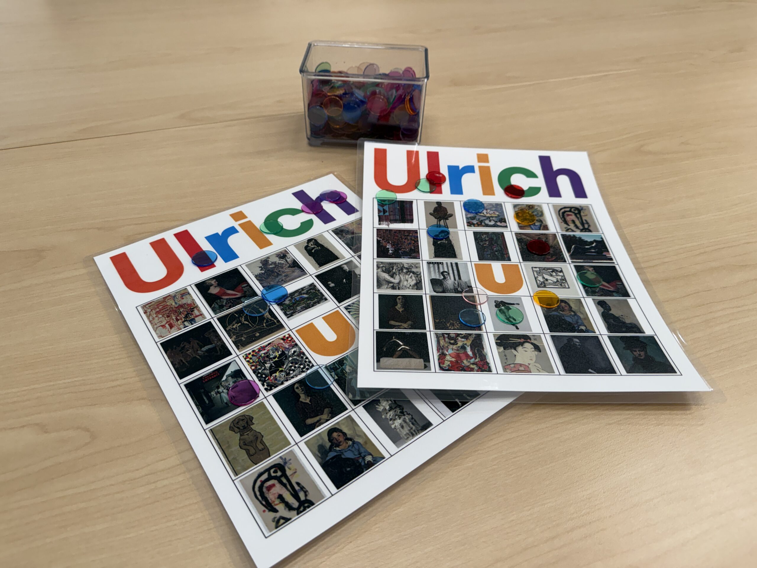 Two Ulrich branded Bingo cards and a container of tiddlywinks on a table.
